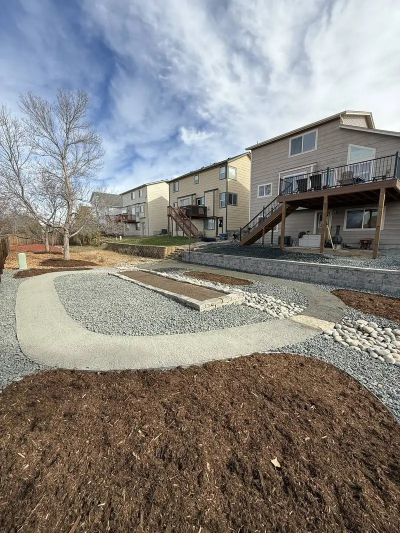 Backyard outdoor living space with fire pit, gravel, and retaining wall by CN Landscaping