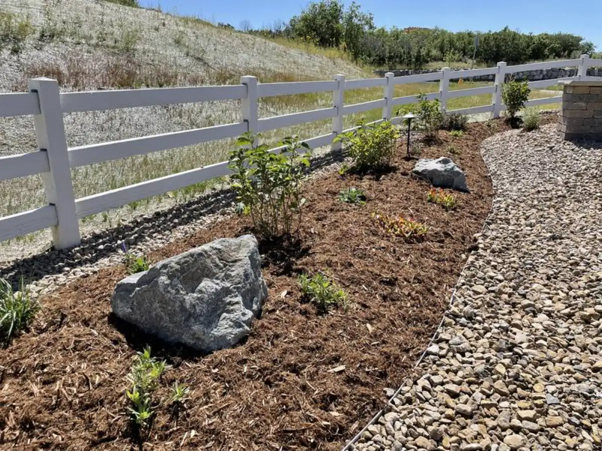Shrub plantings with mulch, boulders, and gravel along white fence in Colorado Springs