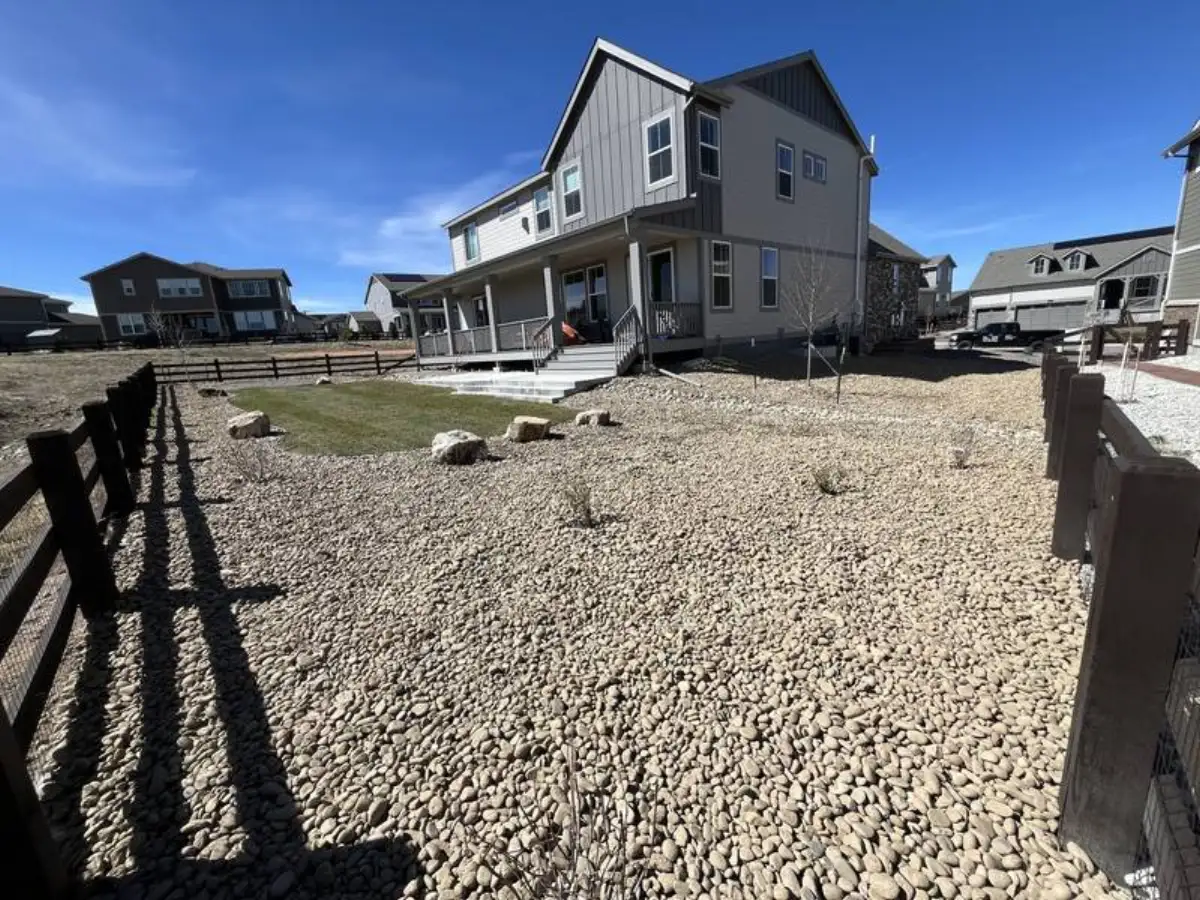 River rock yard with small sod island, boulders, and ranch fence — xeriscaping by CN Landscaping