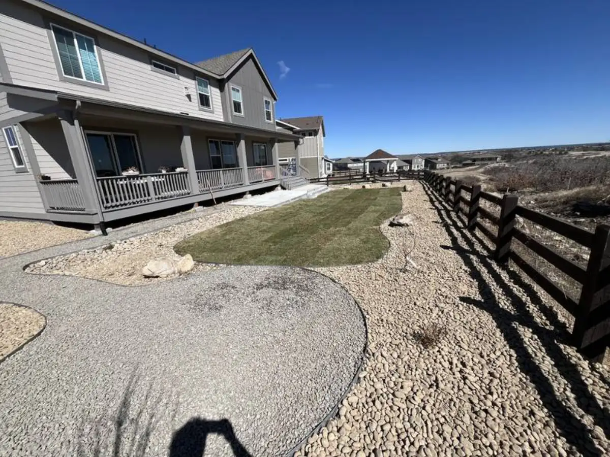 Gravel and sod yard with river rock border and ranch fence — xeriscape design